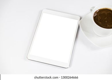 Computer tablet with white empty screen next to coffee. The tablet is on the white table. View from the top. Close-up.