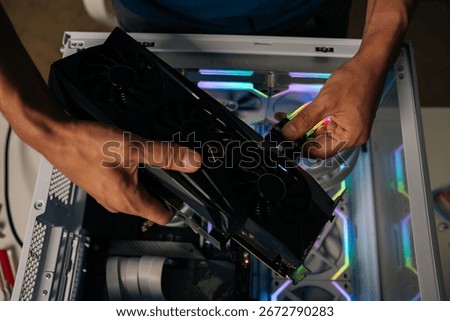 Computer technician installing new graphics card into modern custom-built pc with RGB lighting, enhancing gaming performance and visual experience. Stages of upgrading or assembling desktop computer