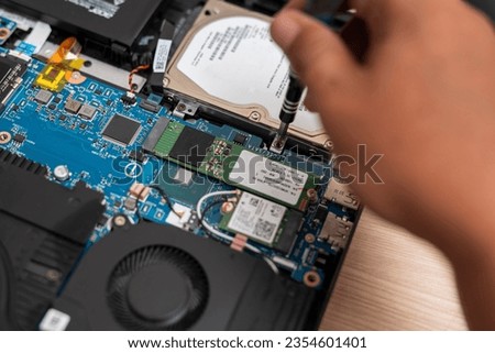 A computer technician removes an SSD drive with a screwdriver. Laptop maintenance and upgrading. Taking off or installing a solid state drive.