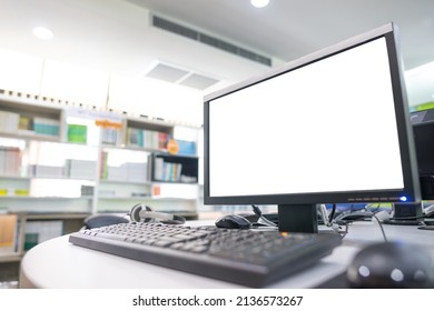 computer and white monitor in a library with many books and shelves in the background.