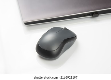 Computer wireless mouse next to a laptop on a white table close-up. electronic personal industry