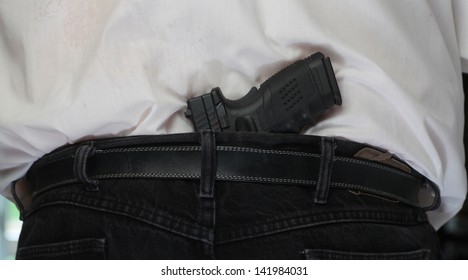Concealed Weapon/Close view of black automatic pistol tucked into man's belt from behind