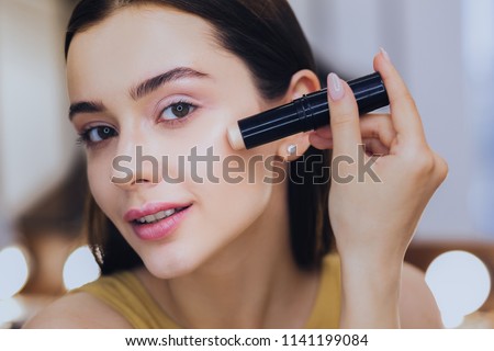 Concealer stick. Charming beautiful woman using concealer stick while putting makeup on