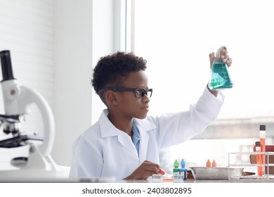 Concentrate African boy in lab coat holds chemical flask for doing science experiment, young schoolboy kid scientist having fun in chemistry laboratory class, little child doing research at school. - Powered by Shutterstock