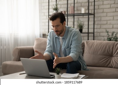 Concentrated 30s Man Sitting On Sofa In Living Room Looking At Computer Screen, Involved In Online Video Call Working Issues Negotiations With Colleagues Or Giving Professional Consultation To Client.