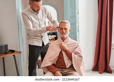 Concentrated Adult Man Making Haircut For His Father At Home With Haircut Machine