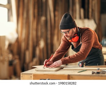 Concentrated adult woodworker marking wooden piece with pencil while working at workbench in joinery studio - Shutterstock ID 1980158282