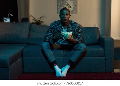 concentrated african american man with popcorn in hands watching tv at home