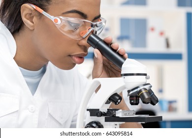 concentrated african american scientist in lab coat working with microscope in chemical lab     - Powered by Shutterstock