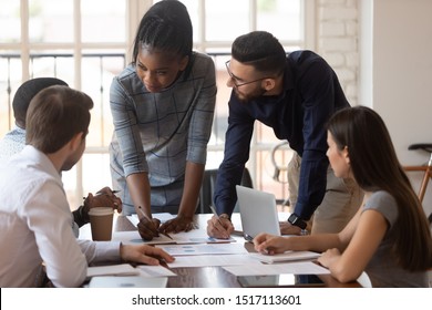 Concentrated african american young female team leader standing near arabian colleague, listening to teammates questions on brainstorming meeting. Diverse group of managers working together at office. - Shutterstock ID 1517113601