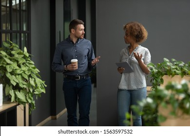 Concentrated african american young trainee asking questions to confident caucasian male team leader, walking together during work pause at coworking office. Couch consulting female intern employee. - Powered by Shutterstock