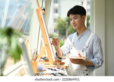 Concentrated asian man painting picture on canvas near window at art workshop. Leisure activity, creative hobby and art concept - Powered by Shutterstock