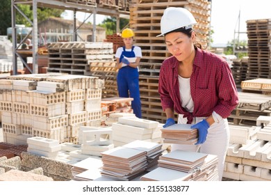 Concentrated Asian Woman Manager Working In A Building Materials Store Is Laying Tiles In A Warehouse