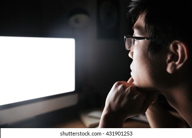 Concentrated Asian Young Man In Glasses Looking At Blank Screen Of Computer In Dark Room