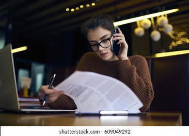 Concentrated attractive female accountant of corporation making distant work checking financial report calling to secretary discussing detail while sitting in coffee shop with laptop computer and wifi - Powered by Shutterstock