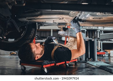 Concentrated auto mechanic male working alone on the floor repairing bottom of the car, look at details, troubleshoot the car. Selective focus. - Powered by Shutterstock