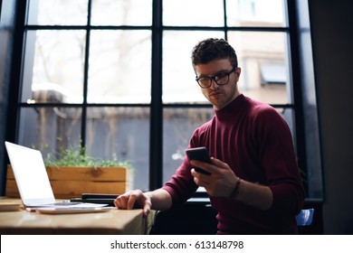 Concentrated Bearded Hipster Guy Watching Streaming Video Via Smartphone Connected To 4G Internet In Coworking Space, Handsome Serious Male Freelancer Reading Text Messages Checking Email On Cellular