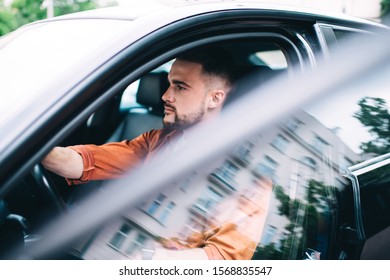 Concentrated Bearded Male Driver In Casual Clothes Sitting With Hands On Wheel In Black Car With Rolled Down Windows Looking Away Attentively