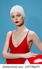 A Concentrated Beautiful Lady In A Swimming Cap, A Red Swimsuit With A Ball On A Blue Background Looks At The Camera. Conceptual Fashion