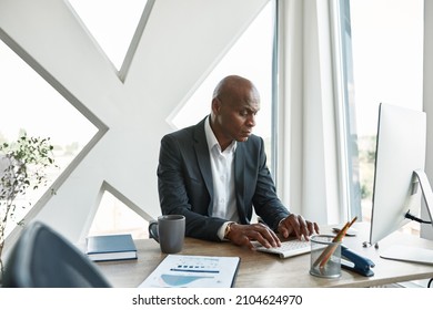 Concentrated Black Male Businessman Typing On Computer During Working In Office. Adult Company Boss Sitting At Desk. Concept Of Modern Successful Man. Idea Of Business Leadership And Management