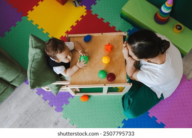 Concentrated boy during SIT classes with educational psychologist holding colored ball for development of sensory sensitivities, top view. Sensory integration therapy - Powered by Shutterstock