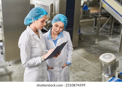 Concentrated busy food manufacturing workers in caps and lab coats analyzing data in clipboard and filling paper after production expertise - Powered by Shutterstock