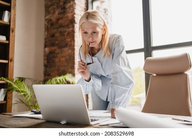 Concentrated caucasian middle-aged mature businesswoman ceo boss typing on laptop, working at office desk with documents, searching surfing web online