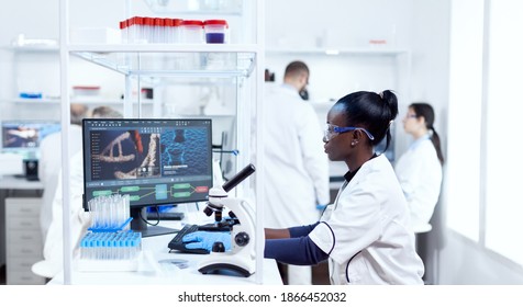 Concentrated Chemist African Researcher Using Computer In Modern Facility. Black Healthcare Scientist In Biochemistry Laboratory Wearing Sterile Equipment.