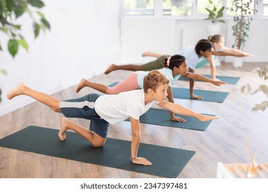 Concentrated children performing asana Dandyamana Brahmanaasana during group yoga course in fitness studio - Powered by Shutterstock