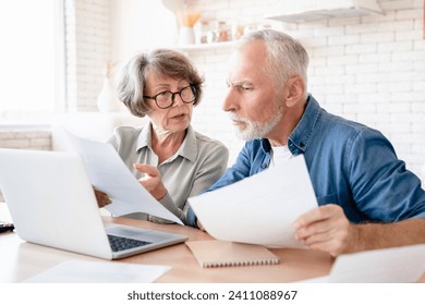 Concentrated concerned european senior old elderly couple spouses grandparents doing paperwork, paying domestic bills, rentals, receiving pension, calculating funds and budget at home kitchen - Powered by Shutterstock