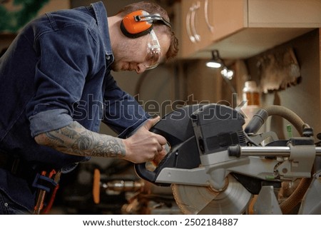 Concentrated craftsman making precise cuts with circular saw in woodworking workshop surrounded by tools and equipment