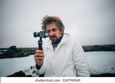 Concentrated creative content creator, videographer or photographer makes video or photo on action camera attached to gimball stabilizator on windy and cloudy day in iceland