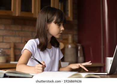 Concentrated Cute Little 9s Hispanic Girl Sit At Table At Home Do Homework Use Laptop With Wireless Internet. Focused Small Teen Child Study Distant On Computer Alone. Online Education Concept.