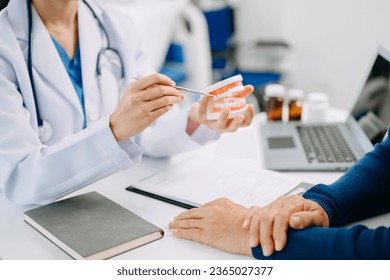 Concentrated dentist sitting at table with jaw samples tooth model and working with tablet and laptop in dental office professional dental clinic. medical doctor working 