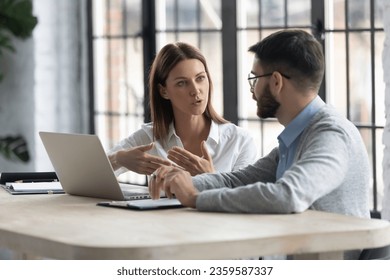 Concentrated diverse businesspeople sit at desk talk brainstorm at office meeting using laptop, focused colleagues consider discuss business ideas, work at computer at briefing, collaboration concept