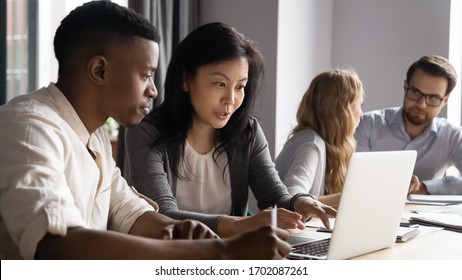 Concentrated diverse sit at desk brainstorm working on laptop together, focused multiracial coworkers talk discuss business ideas cooperate using computer at office briefing, collaboration concept - Shutterstock ID 1702087261