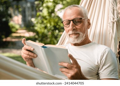 Concentrated dreamy old senior elderly caucasian grandfather man relaxing resting in hammock while reading book outdoors in park garden forest - Powered by Shutterstock