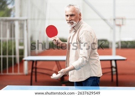 Concentrated elderly man holding racket and ball getting ready to serve while playing table tennis outdoors