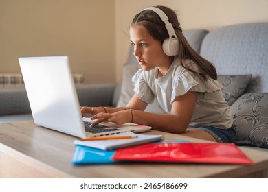 Concentrated Elementary Age Girl Using Laptop And Headphones For An Online Class At Home, She Is Interacting In A Virtual Class. Real Little Girl Using Technology For School Education.Homeschooling - Powered by Shutterstock