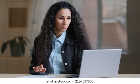 Concentrated female arab businesswoman multitasking worker accountant calculate costs credit balance use laptop online payment e-commerce complete financial report papers write signature sign document