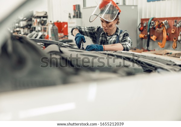Concentrated female automotive technician using a\
pair of vise grips