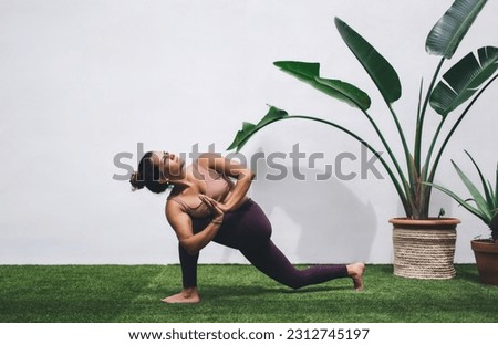 Concentrated female in casual tracksuit practice hatha yoga for reaching relaxation and inspiration, calm flexible woman standing in asana breathing and feeling vitality and muscular stretching