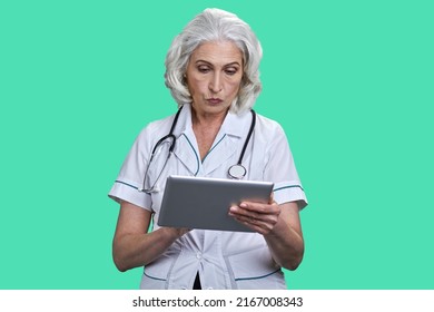 Concentrated Female Doctor With Stethoscope Looking At Digital Tablet Pc. Medical Specialist Working With Computer Tablet On Color Background.