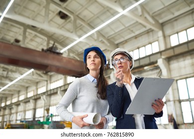 Concentrated female inspector in hardhat examining unfinished industrial building and pointing at construction features to forewoman