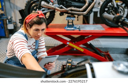 Concentrated female mechanic with digital tablet reviewing information of motorcycle on garage - Powered by Shutterstock