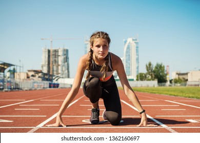 Concentrated female teen athlete in sportswear with fitness tracker on her wrist preparing for run on track at stadium