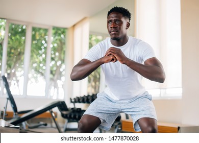 Concentrated fit African American man in sportswear warming up and doing squat exercise during workout. Young sportsman squatting in gym 