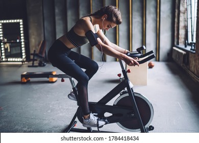 Concentrated fit female in sportswear with dark braided hair burning calories on spin bike and listening to music in headphones - Shutterstock ID 1784418434