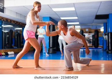 Concentrated girl mastering self defence techniques in sparring with man in gym, using painful supinating wristlock to hold opponent
