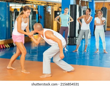 Concentrated girl mastering self defence techniques in sparring with man in gym, using painful supinating wristlock to hold opponent